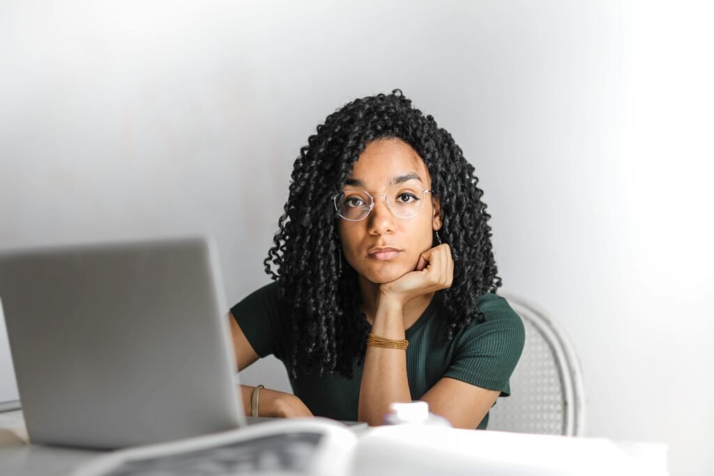 Woman resting her chin by a laptop, thinking about her money scripts