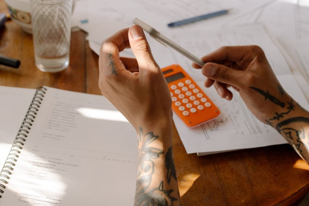Tattooed hands with an orange calculator over loan papers, working out private mortgage insurance costs