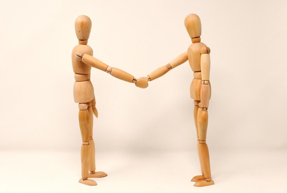 Wooden figures shaking hands to represent rate negotiation with a client