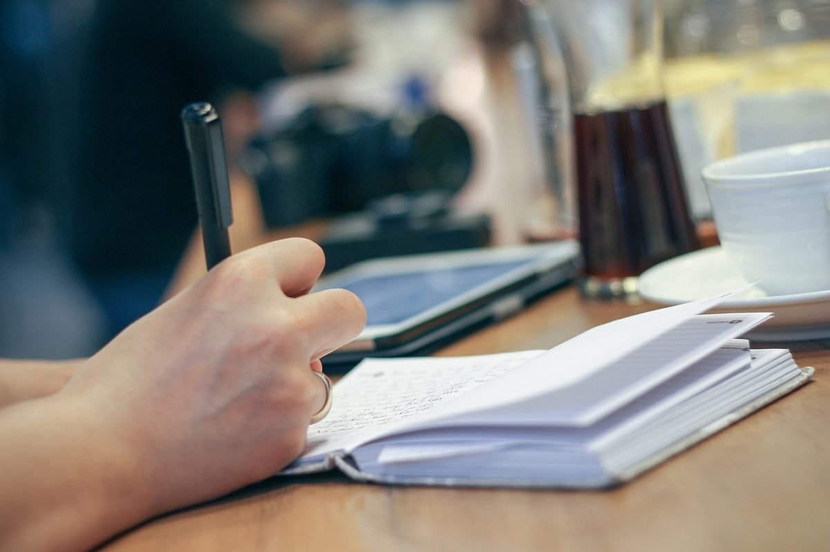 Hand writing in a notebook while working out why budgets fail